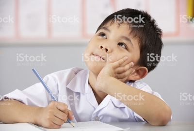 Male Student Working At Desk In Chinese School Classroom Looking Thoughtful