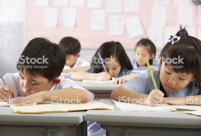 A Group Of Students Working At Desks In A Chinese School Classroom Writing In Their Books